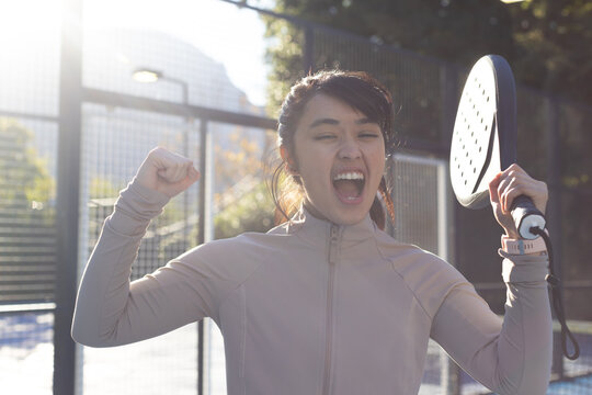 Female player cheering raising fist holding solid paddle, wearing smartwatch on fenced paddle court