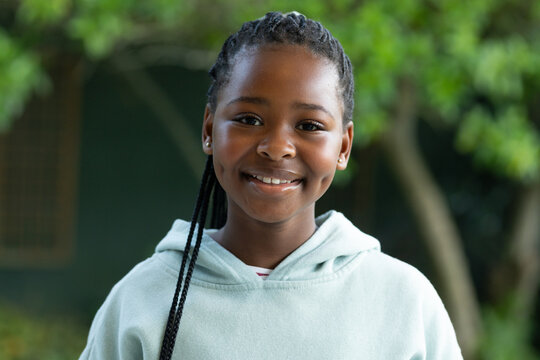 Female youth of African descent smiling outdoors near wall showing braids mint hoodie stud earrings