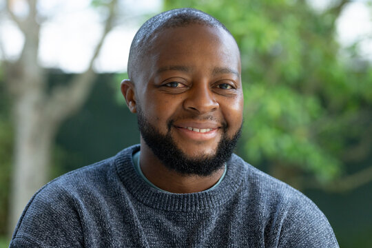 Mature African man smiling and facing camera in garden, showing undershirt collar and grey sweater