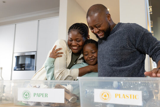 African family hugging and sorting recycling at kitchen counter with PAPER and PLASTIC bins