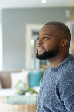 mature African American man gazing left in lounge in gray sweater near woven table, copy space