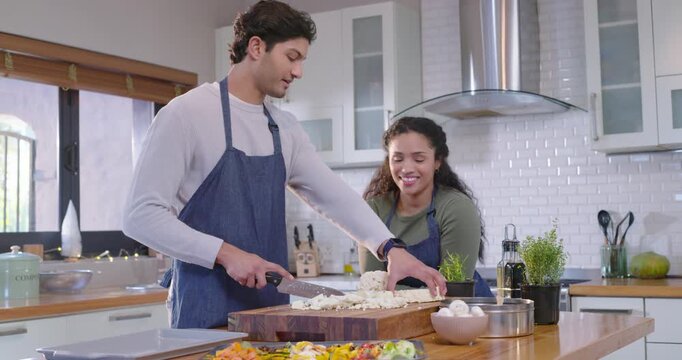 African American couple prepping at island, man chopping cauliflower with knife, woman laughing