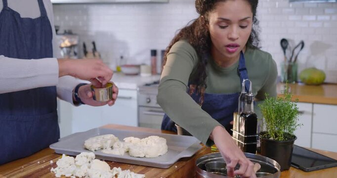 African American cooks, after spice tin reach, tapping turmeric on cauliflower to roast in kitchen