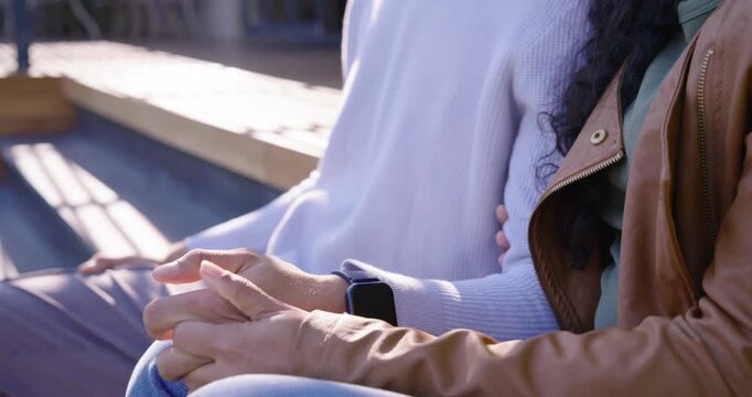 Diverse couple sitting on wooden steps as camera pulling back from linked hands, smiling together