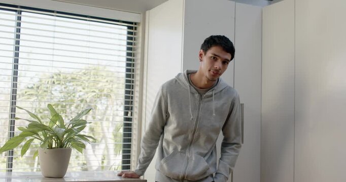 African American man in hoodie glancing, straightening at counter by plant, crossing arms, posing