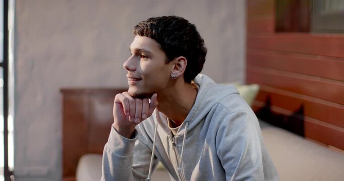 African American man in gray hoodie sitting on couch, camera closing in, smiling, engaging camera