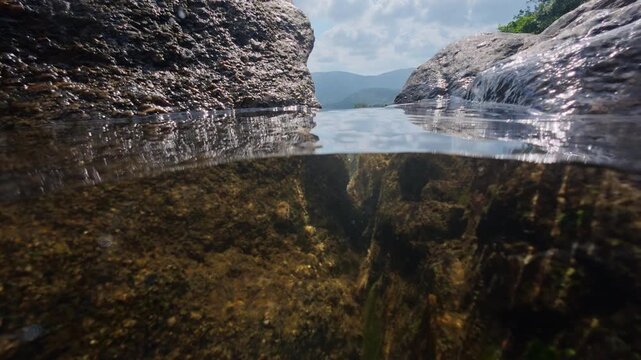 Split level view at Na Muang Waterfall 2 on Koh Samui, Thailand, showing crystal clear freshwater above and below the surface between granite rocks.