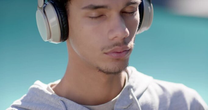 African American man in gray hoodie placing headset, closing eyes, listening closely outdoors