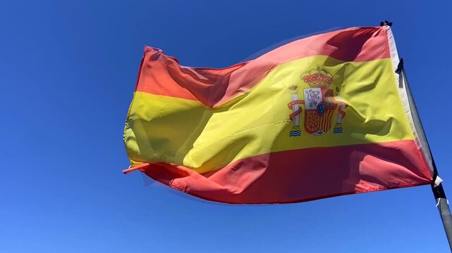 Spanish flag waving in the wind against a clear blue sky, 4K.