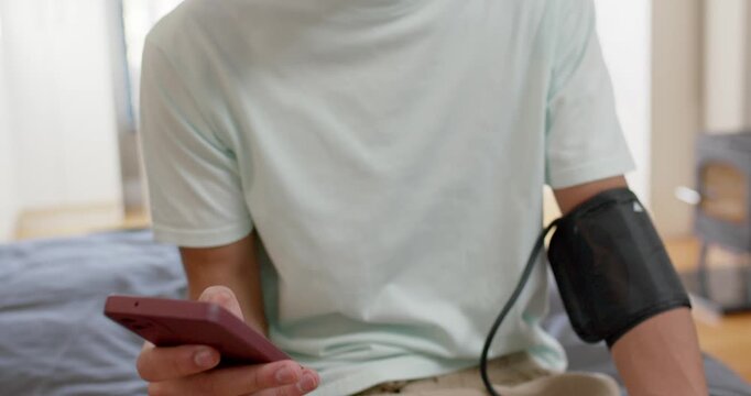 African American man sitting on bed cuff inflating steadying monitor checking red phone tracking BP