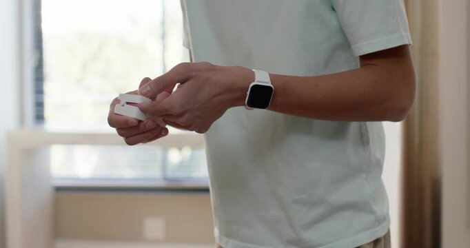 African American man in 20s standing at home counter with smartwatch, opening case, removing earbud