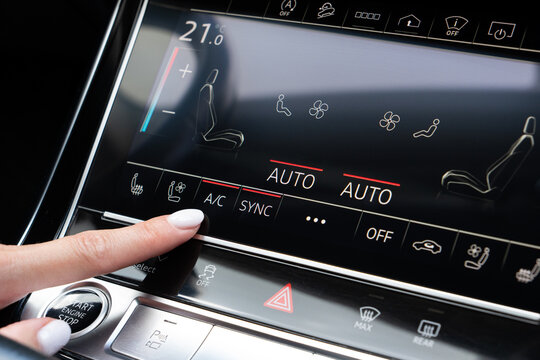 Woman finger pressing AC button on car touch screen climate control system