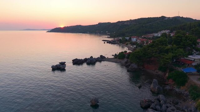 Drone shot of Loutra beach rocky shoreline with resort and hotels, Agia Paraskevi Pine forest at sunset, Kassandra Peninsula, Aerial