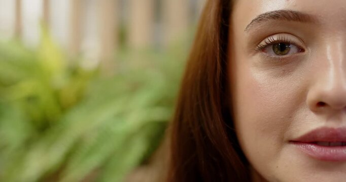 Adult female shifting neutral to broad smile after off-camera cue on porch plants slats, copy space