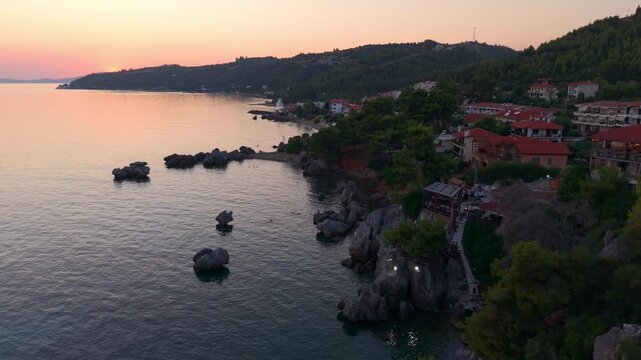 Aerial view of a traditional greek taverna on rocky cliff turquoise sea shore at sunset, Loutra beach and Agia Paraskevi Pine Forest, Kassandra Peninsula