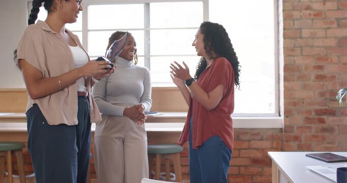 Diverse female team celebrating award handoff at loft, clapping around woman holding glass trophy