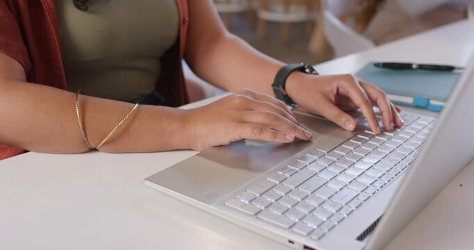 Adult woman opening silver laptop, typing, donning white headphones, working at white table in cafe