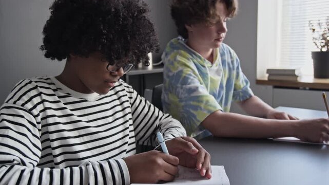 African American and Caucasian teenagers sitting at desk, writing in notebooks during lesson. Footage for educational marketing and school promotional videos