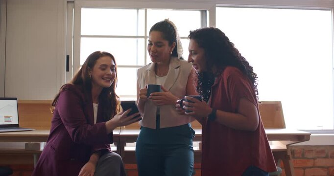 Office female coworkers, left woman showing smartphone, colleagues leaning with mugs during break