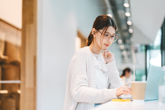 Young adult business asian woman using laptop at co working space wear eyeglasses, wireless headphones urban lifestyles with modern digital technology
