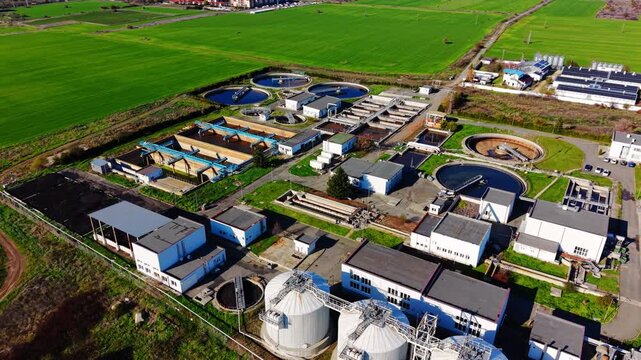 Aerial view of a treatment plant with storage silos, Bulgaria. Drone shot of cylindrical tanks, solar panels, green fields and access roads at a rural site.