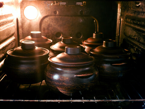 Baking delicious meat and vegetable stew in traditional ceramic clay pots inside the hot oven. Cozy homemade cooking process concept.