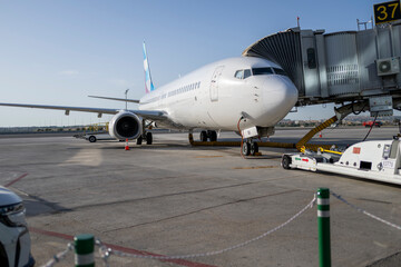 Fototapeta premium Commercial passenger aircraft connected to jet bridge at airport gate during boarding preparation with ground support equipment ready for international travel and modern aviation operations