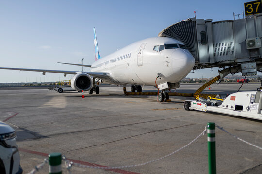 Commercial passenger aircraft connected to jet bridge at airport gate during boarding preparation with ground support equipment ready for international travel and modern aviation operations