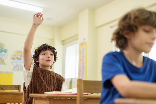 Young student raises a hand to answer a question in the classroom, representing active learning, participation, confidence, and engagement in primary education.