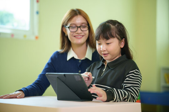 Teacher guides a young student using a digital tablet in the classroom, encouraging interactive learning, creativity, digital skills, and confidence in primary education.