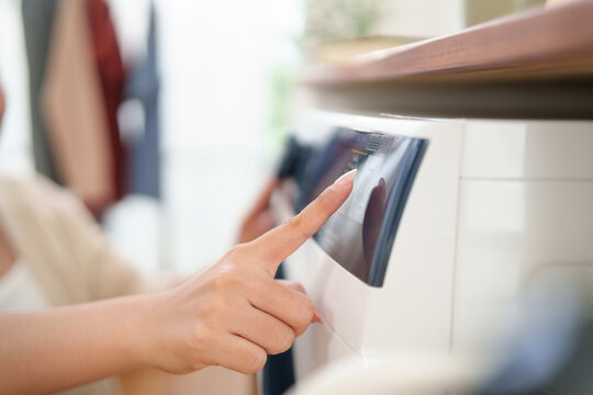 Close-up of a hand pressing the control panel on a washing machine, highlighting smart home technology, efficient laundry management, and modern household convenience.