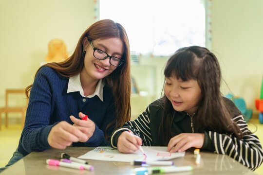 Teacher supports a young child during a creative drawing activity, encouraging confidence, imagination, and joyful learning in a colorful classroom.