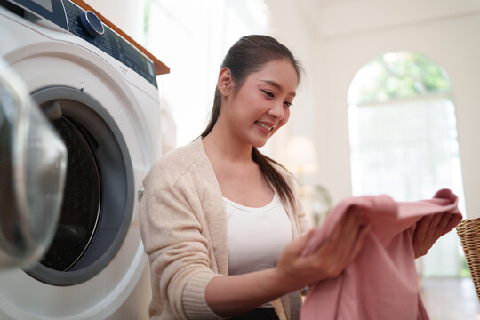 Smiling woman checks freshly washed clothes beside a washing machine, reflecting fabric care, freshness, cleanliness, and comfortable modern home living.