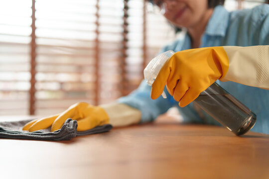 Woman sprays cleaner and wipes a wooden table with a microfiber cloth, promoting hygiene, sanitation, and efficient household cleaning in a modern home.