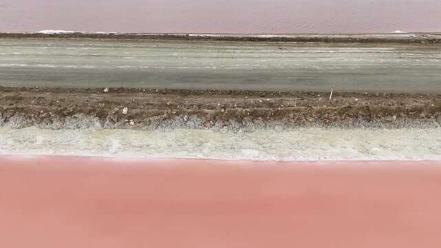 Cinematic aerial footage of vibrant pink salt evaporation ponds in Namibia. A unique industrial and natural landscape of colorful salinas stretching to the horizon.