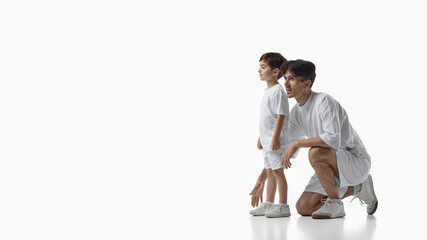 Father kneeling beside young son watching something ahead on white background. Concept of shared...
