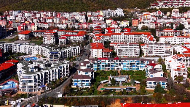 Residential apartment complex, Bulgaria. Aerial view of multistory buildings with red and white facades, pools and forested hillside behind.