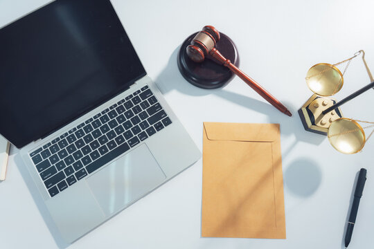 Legal Desk Arrangement: A laptop, gavel, scales of justice, an envelope, and a pen are neatly arranged on a desk, symbolizing legal proceedings and justice.