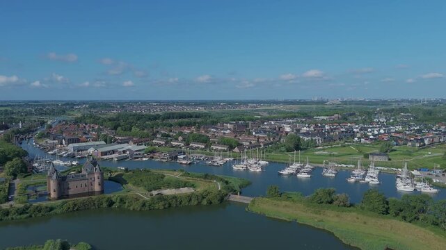 Drone view moving from right to left over Muiden, with the castle and harbor in the foreground and the Amsterdam skyline visible in the distance.