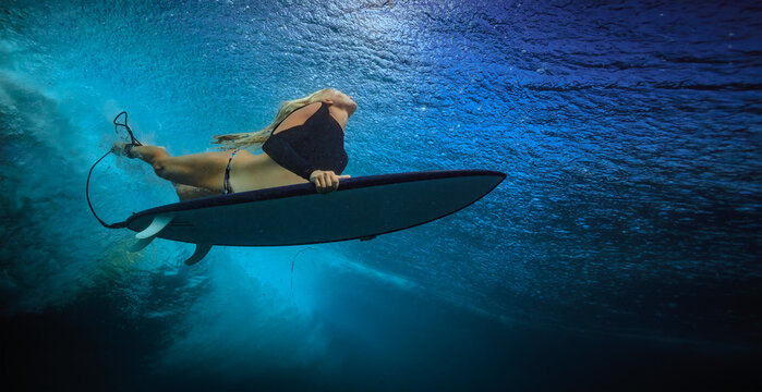 Low angle underwater shot of blonde female surfer paddling on board