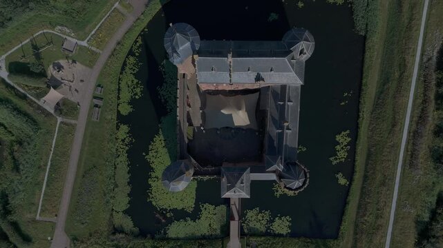 Aerial top down view of a historic castle surrounded by a moat, filmed with a drone ascending upward above the building on a clear day.