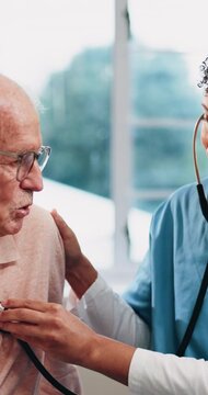 Nurse, senior and checkup with stethoscope for healthcare visit or breathing exam in home. Female person, health worker or listening to heart beat with elderly man or patient for medical aid or help