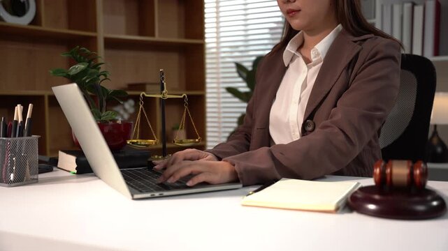 Lawyer at Work: A professional woman in a suit typing on a laptop in a law office, surrounded by legal books and scales of justice.