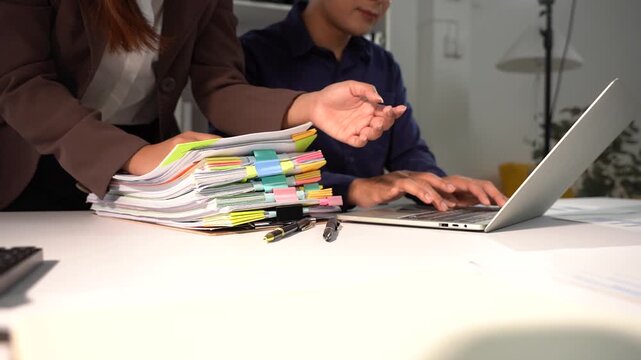 Teamwork in office: Two business professionals collaboratively work on a laptop with a stack of documents, highlighting focused effort and shared responsibility.
