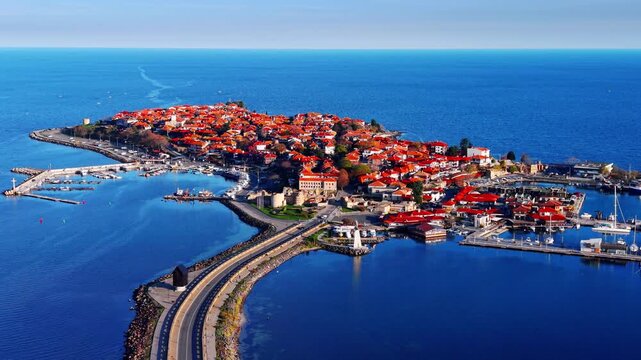 Nessebar peninsula with causeway, Bulgaria. Drone shot of the historic town surrounded by deep blue sea, connected to shore by a narrow road.