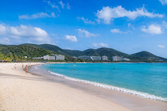 Long white Hainan beach curving beside clear turquoise sea and green hills.generative AI