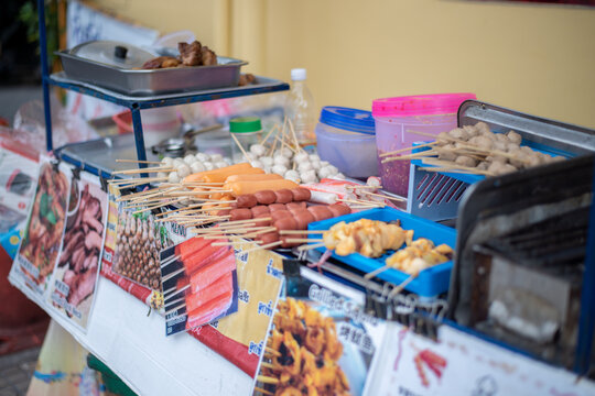 Close-up of a popular street food stall in Bangkok, Thailand, showcasing a selection of meatball and sausage skewers, a famous local Asian snack.