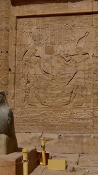 Ancient falcon statue representing Horus stands against temple walls covered in hieroglyphs at the Edfu Temple Complex, symbolizing power and divine protection. Egypt