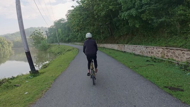 Person Cycling on a Road Beside a Lake