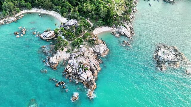 Cinematic aerial drone view of tropical beach with granite coastline, turquoise waters, hidden sandy coves and lush island paradise scenery below